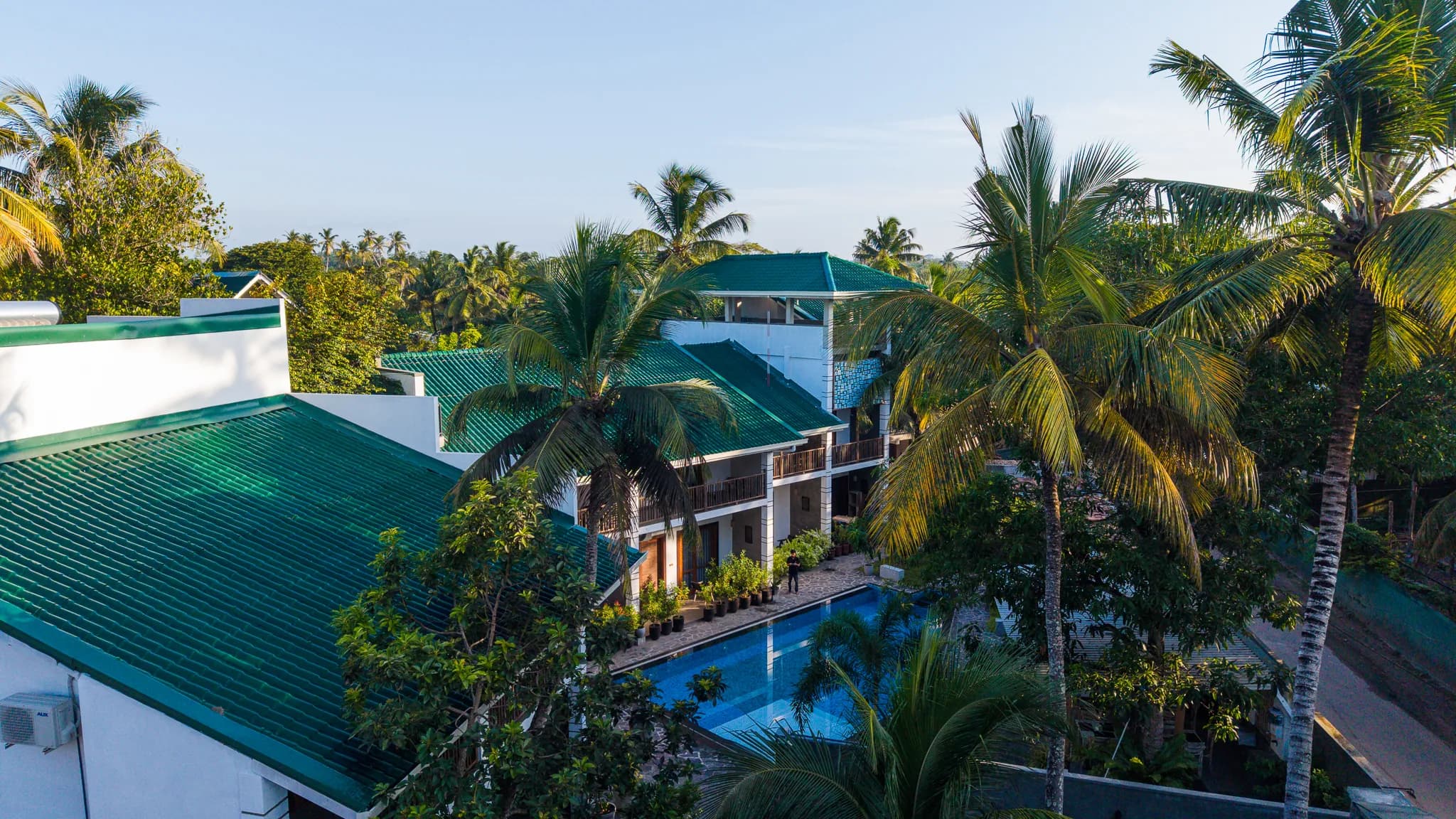 Aerial view over coconut palms to the hotel's green roofs and pool