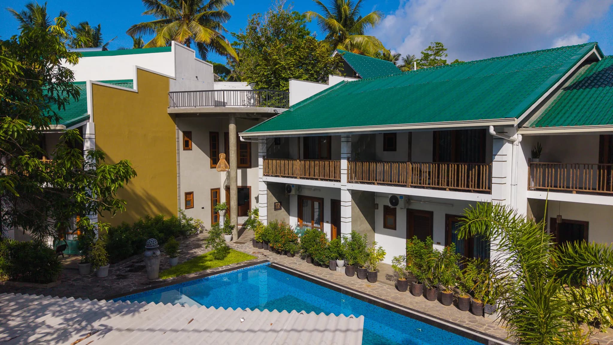 Aerial view of The Lavish Haven: green roofs, the pool and surrounding palms