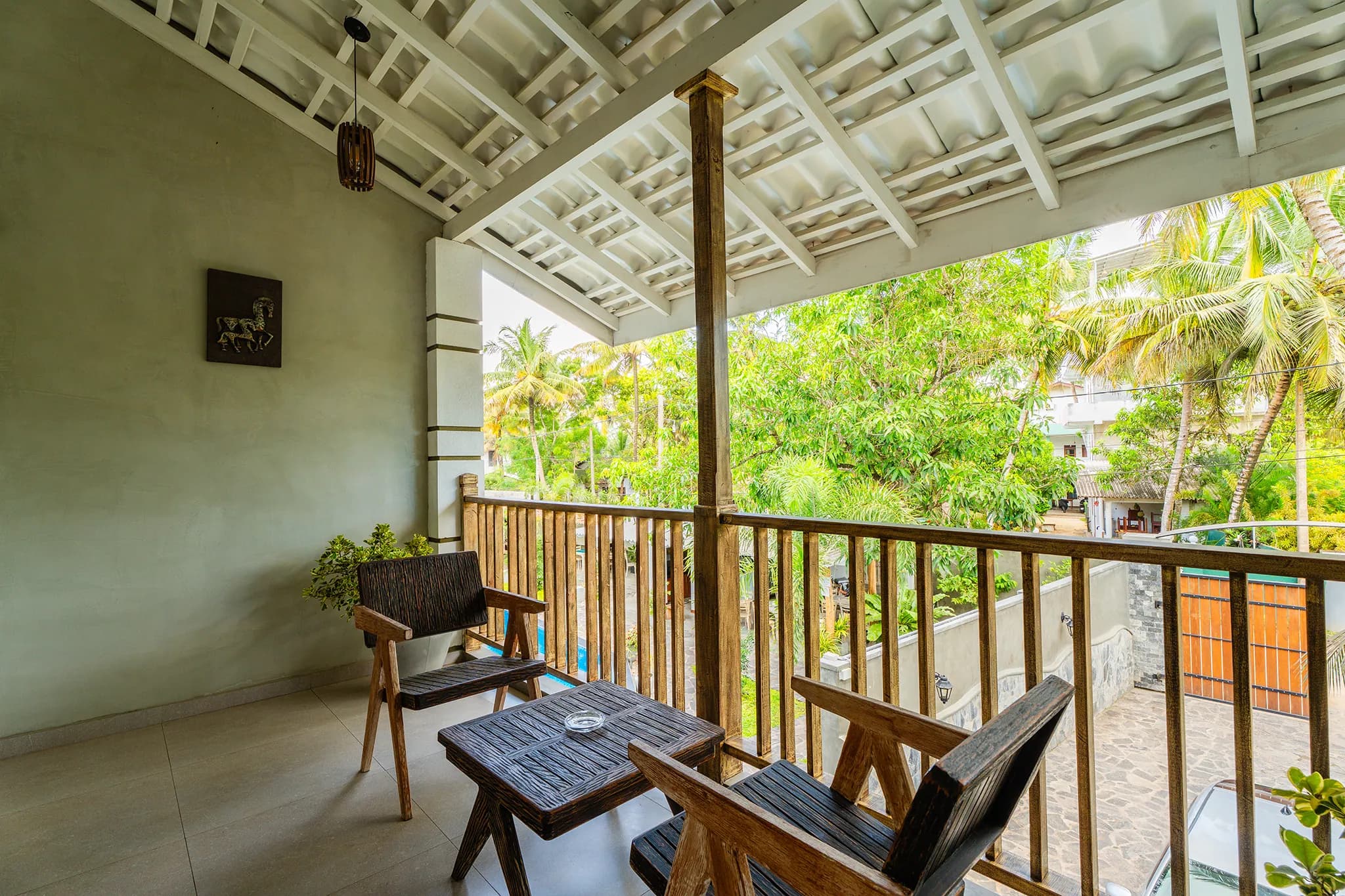 Covered first-floor balcony with timber chairs looking over the garden and pool